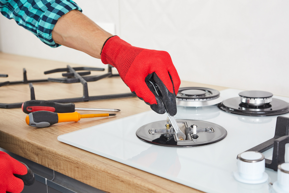 Men's hands repair the hob with a tool. The technician adjusts the burner of a gas stove.